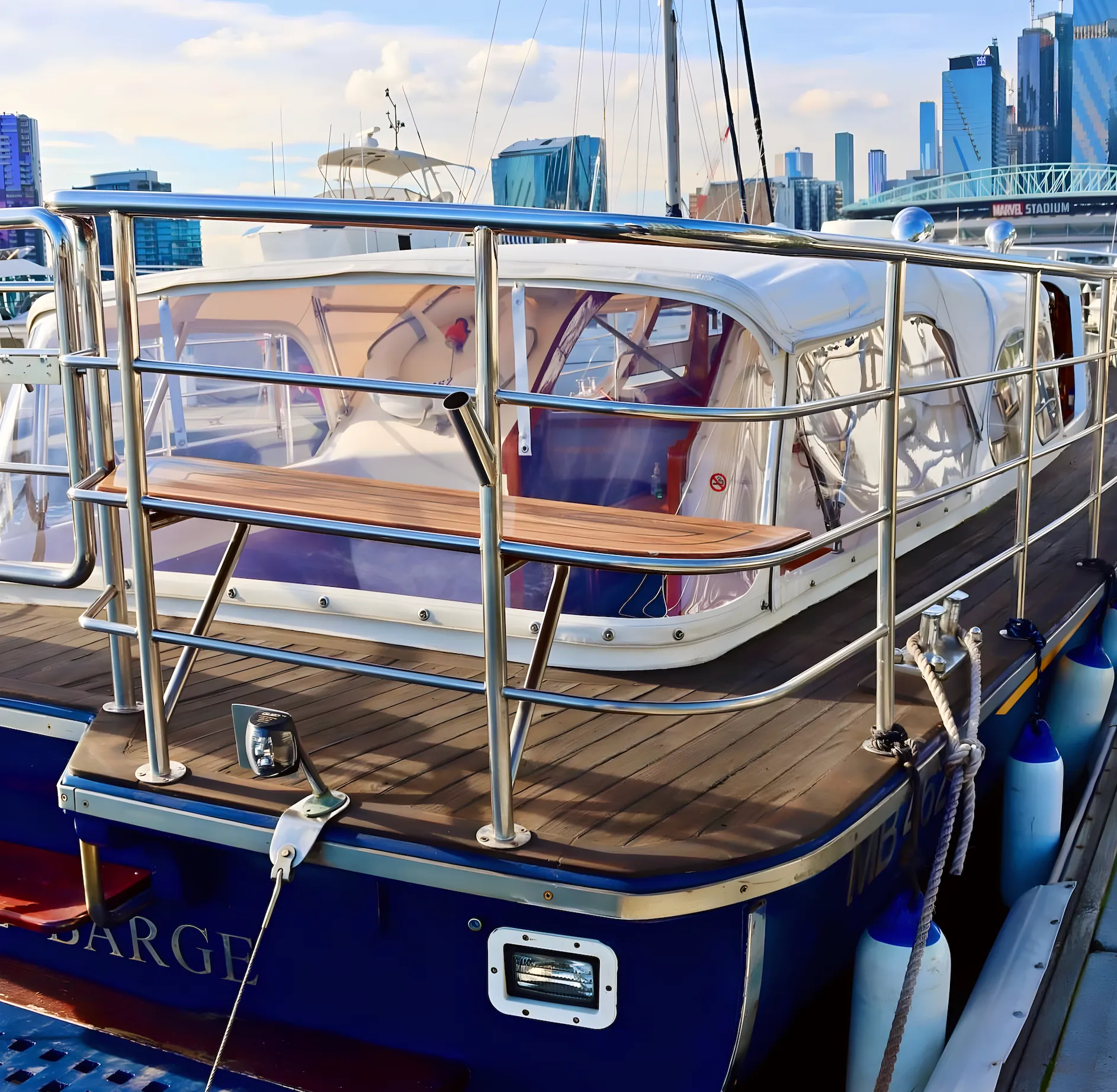 Elizabeth Anne's stern deck with teak table and rails, Marvel Stadium and the city skyline behind