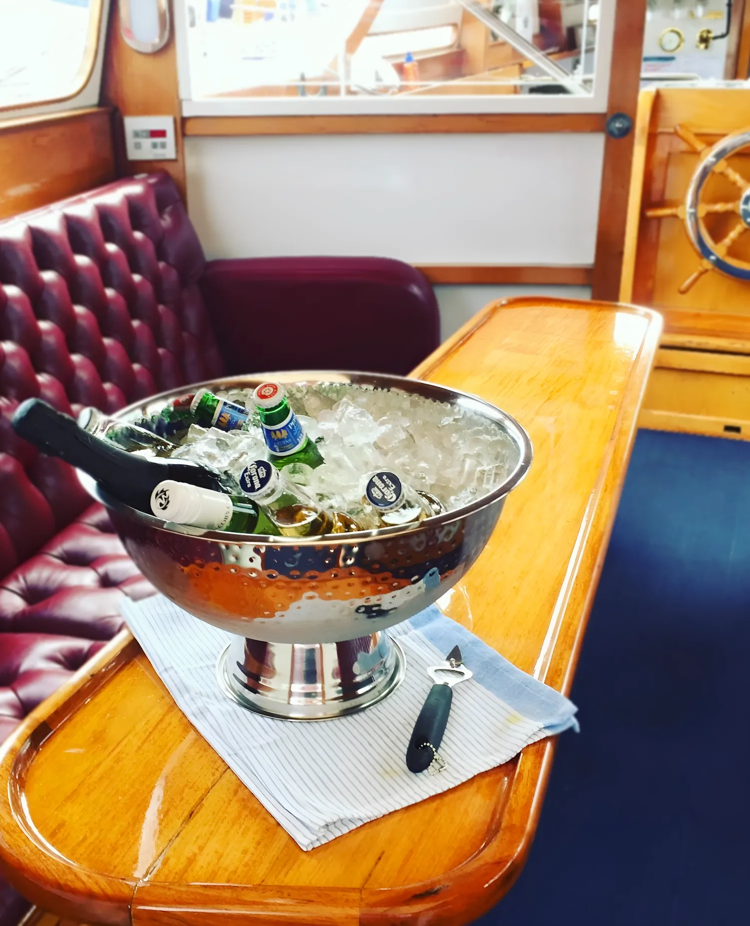 A hammered-silver ice bowl of drinks on the timber saloon table, the ship’s wheel behind